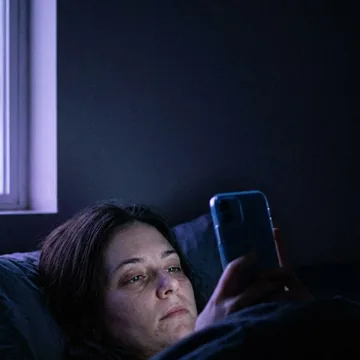 A woman in bed at night, face lit by her phone